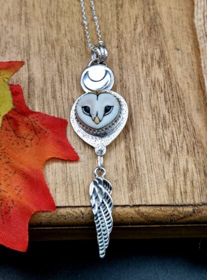 A silver owl pendant. The owl face is crowned with a moon, and features a silver feather charm.